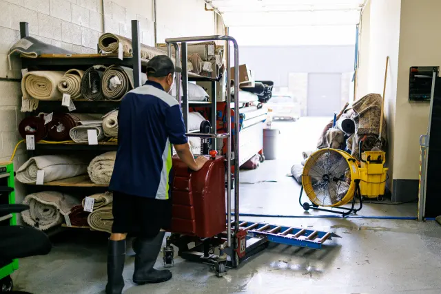 Technician moving a wrapped rug past shelves of tagged rugs
