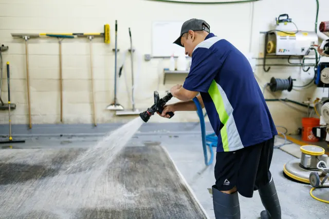 Technician rinsing a rug with a spray wand to flush out silt