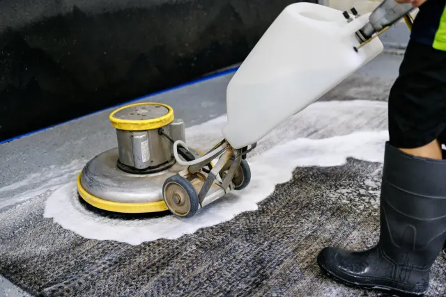 Rotary scrubber cleaning a gray rug with foam