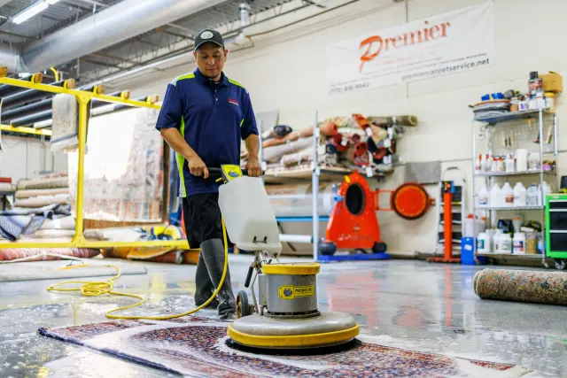 Technician scrubbing an Oriental rug with a rotary machine on the wash floor